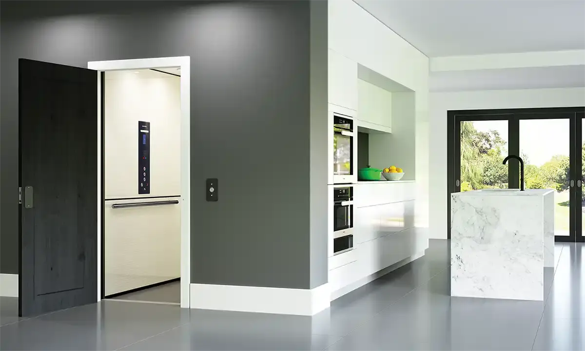 Open residential elevator integrated into a modern kitchen with marble island and dark cabinetry