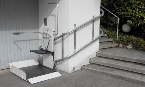 A custom twin rail incline platform lift installed along the wall of an outdoor stone staircase.