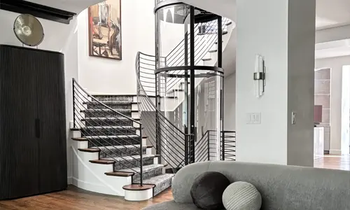 A black-framed winding drum elevator installed in the center of a multilevel staircase of a residential home.