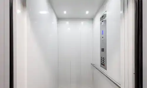 Bright white elevator interior with smooth wall panels, ceiling lights, and a stainless‑steel control panel on the right.