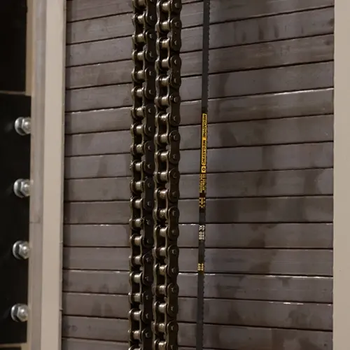 Geared chain drive system with dual vertical lift chains running along a tracked guide surface, showing the closely linked metal chain segments and tensioned alignment used to raise and lower the elevator platform.