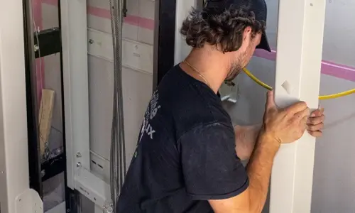 Elevator technician installing and securing vertical guide rail components inside a residential home elevator shaft during lift installation.