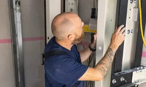 Elevator technician aligning and securing vertical guide rails inside a residential home elevator shaft during installation.