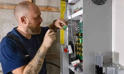 Elevator technician performing electrical maintenance on a residential elevator control cabinet, adjusting wiring and components for safe and reliable lift operation.