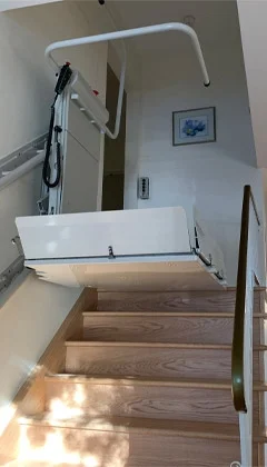 Delta inclined platform lift at the top landing of a wooden staircase.