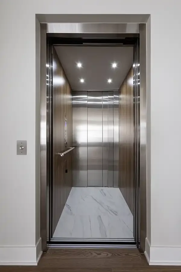 Residential elevator with stainless steel doors, wood-paneled interior, recessed ceiling lights, and marble flooring