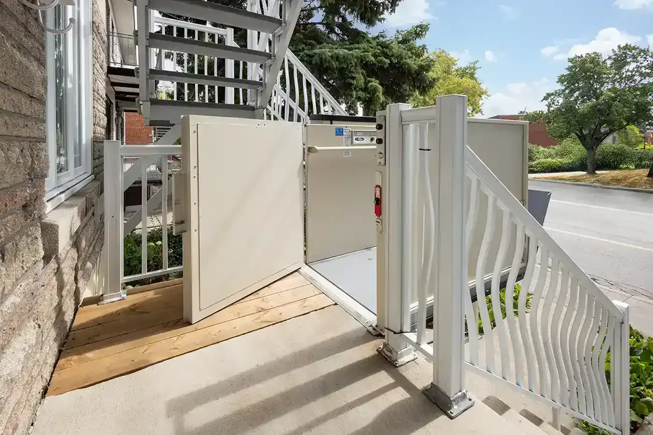 Outdoor wheelchair platform lift installed at a residential entrance with open safety gates