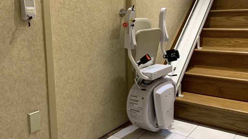 Straight stair lift attached to a rail along a wooden staircase.