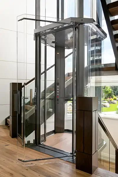 Glass residential elevator with clear panels and a sleek metal frame installed beside a modern staircase.