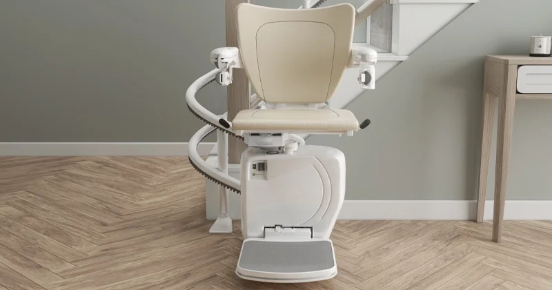 Curved stairlift with upholstered seat, safety armrests, and footrest installed on a residential staircase for home accessibility.