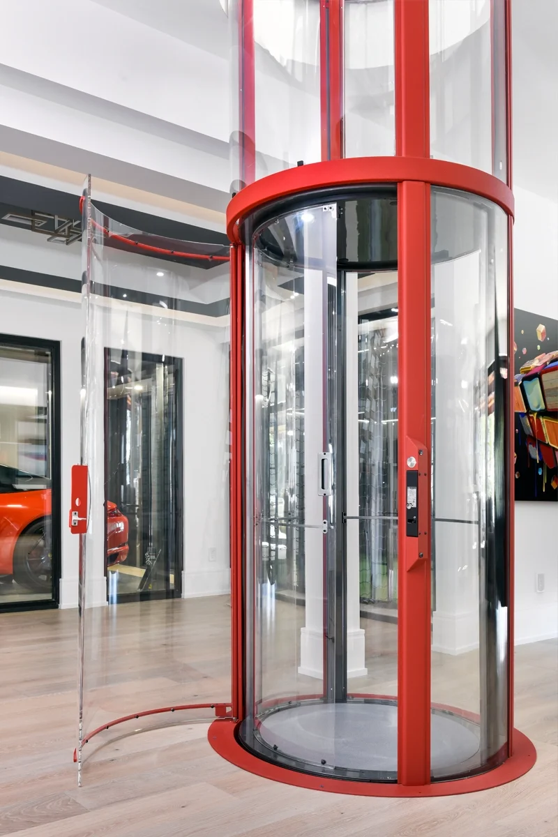 Red panoramic glass residential elevator with cylindrical design, transparent walls, and modern interior installed in a luxury home.