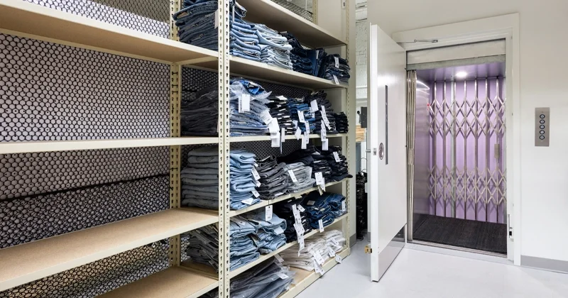 Commercial material lift in a retail stockroom with open service elevator door, used for transporting merchandise and inventory between floors.