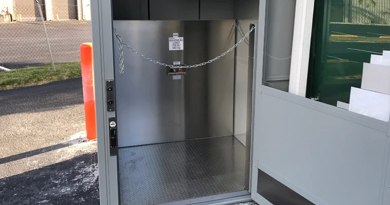 Commercial material lift with stainless steel interior, open door, chain safety barrier, and diamond plate platform designed for transporting goods between levels.