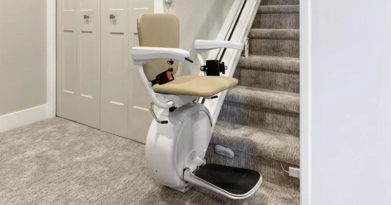 Residential stairlift with upholstered seat, safety armrests, footrest, and rail system installed on a carpeted indoor staircase for home mobility and accessibility.