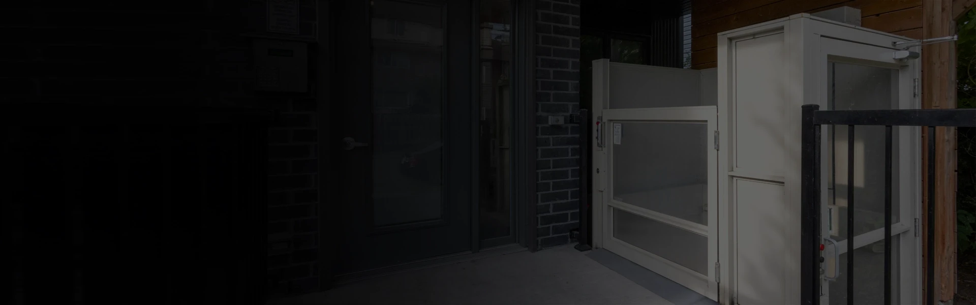 Outdoor wheelchair lift installed beside a building entrance, featuring a gated platform and safety panels.