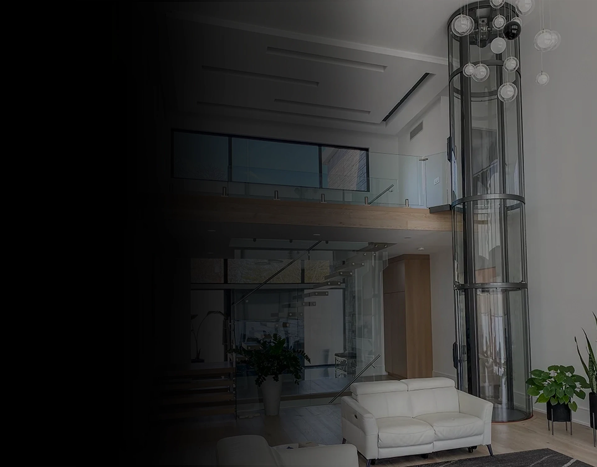 Glass cylindrical residential elevator extending through a multi-level modern home with chandelier lighting