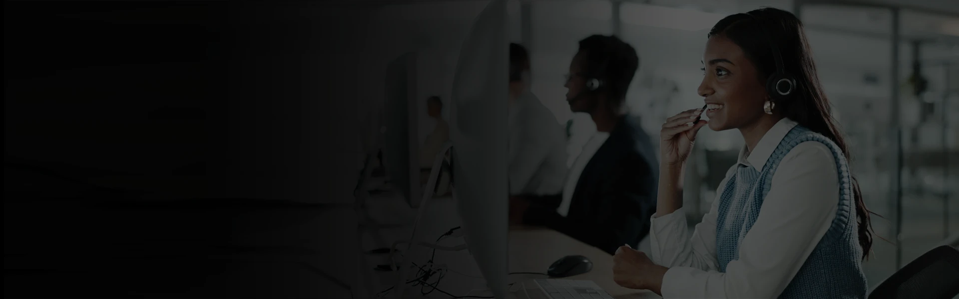 Call center workspace with customer support agents wearing headsets and working at computer stations in a modern office environment, representing professional customer service and contact center operations.