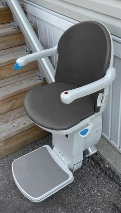 Gray seat outdoor stairlift installed along a wooden staircase.