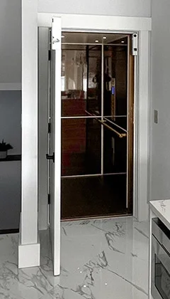 Open residential elevator with a white door, glass panels, and a metallic handrail, in a modern interior with marble flooring.