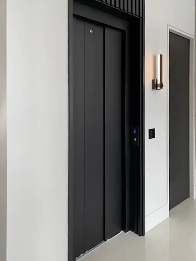 Modern residential elevator with matte black sliding doors, minimalist wall call button, and contemporary interior design integrated into a luxury home hallway.