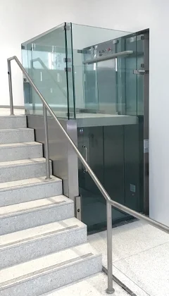 Glass panel and stainless steel vertical platform lift installed alongside a staircase.