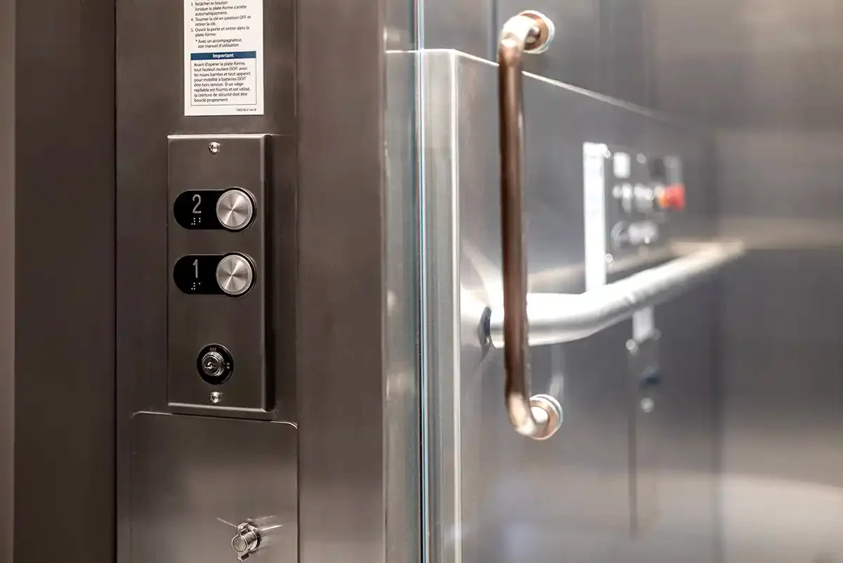 Close-up of elevator control panel with floor buttons, glass wall, and stainless steel handrail