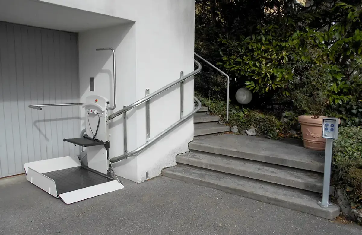 Outdoor inclined wheelchair platform lift installed beside a short exterior staircase at a residential entrance