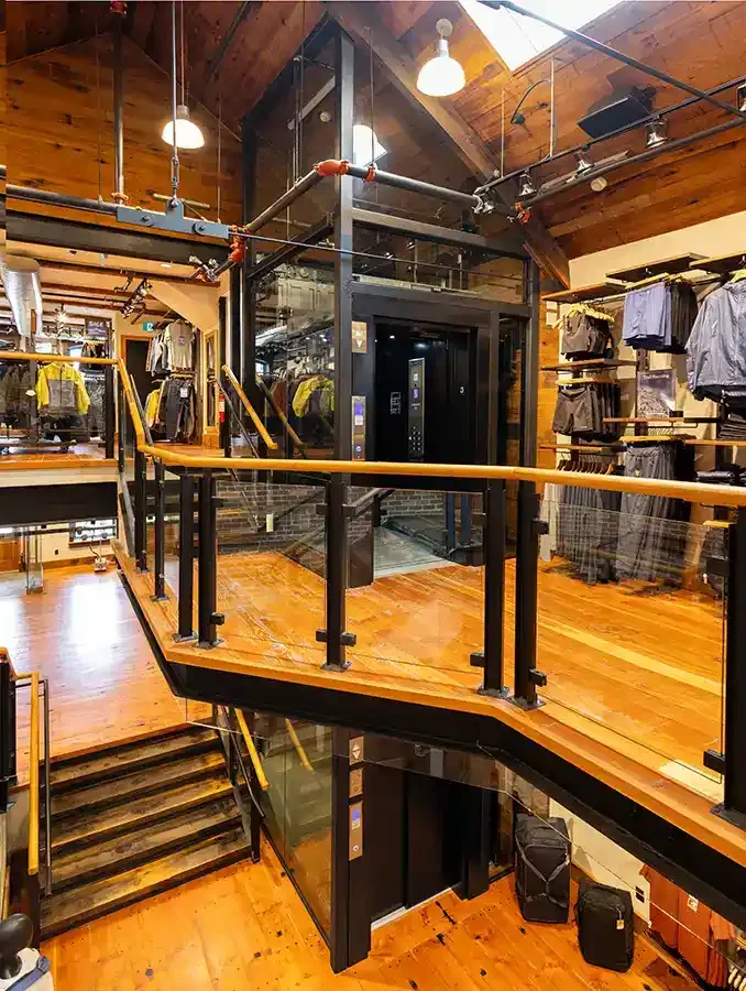 Industrial loft interior with a glass residential elevator, wood floors, exposed beams, and surrounding retail displays