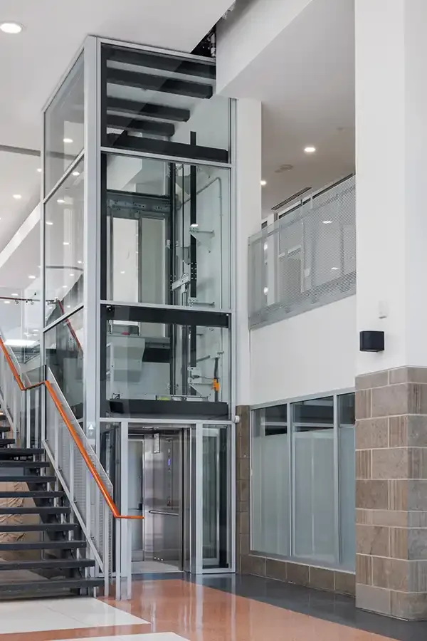 Glass commercial elevator spanning multiple floors beside a staircase in a modern atrium