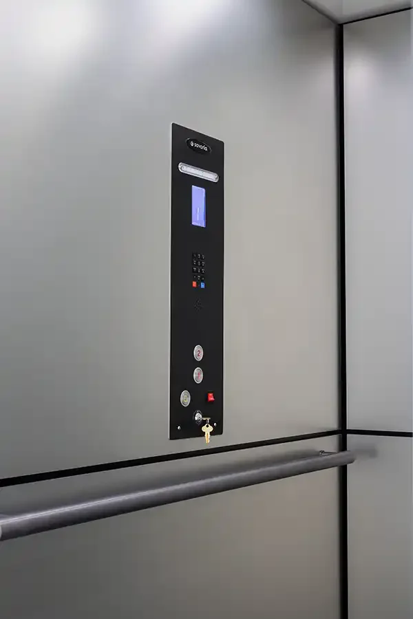 Residential elevator interior with sleek control panel, handrail, and light gray wall panels
