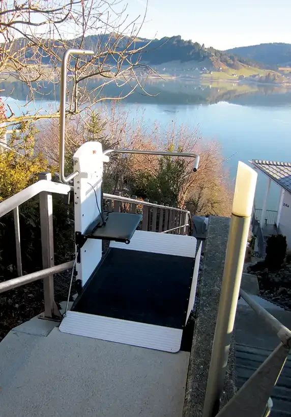 Outdoor wheelchair platform lift installed on a stair landing overlooking a lakeside landscape