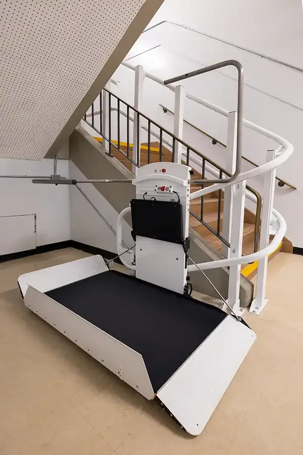 Inclined wheelchair platform lift deployed at the base of a curved commercial staircase with safety rails and folded ramp edges