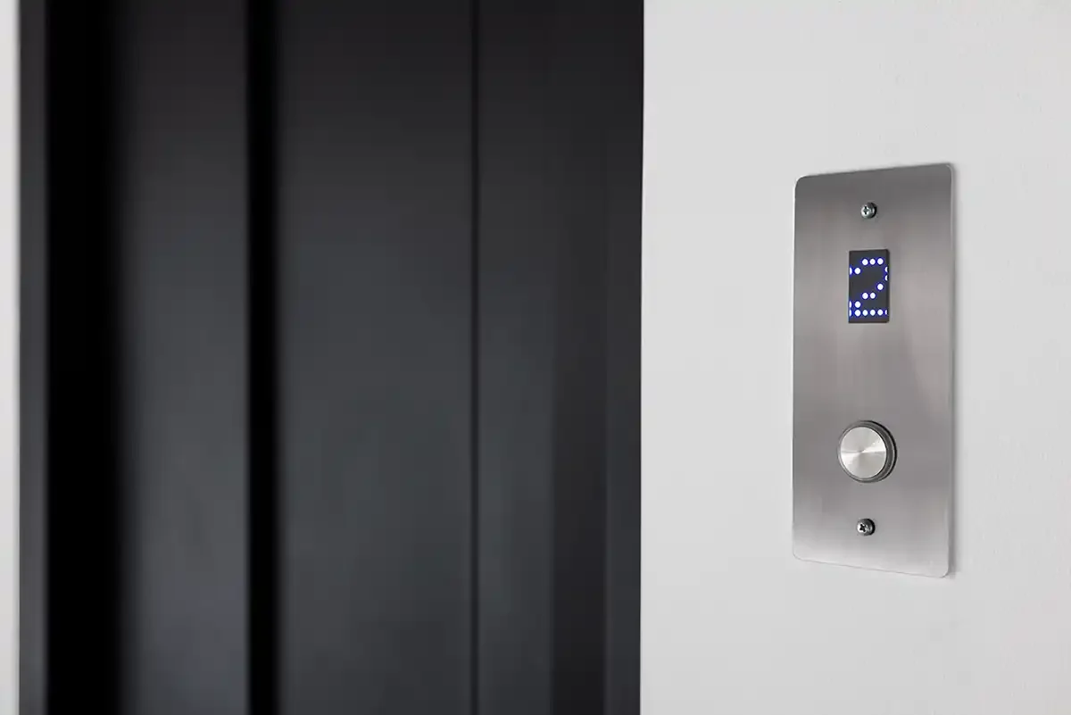 Elevator call button with digital floor indicator mounted beside closed elevator doors