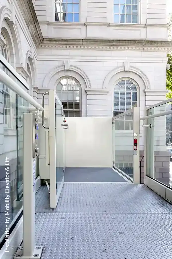 Outdoor commercial wheelchair platform lift with safety gates beside a historic building façade