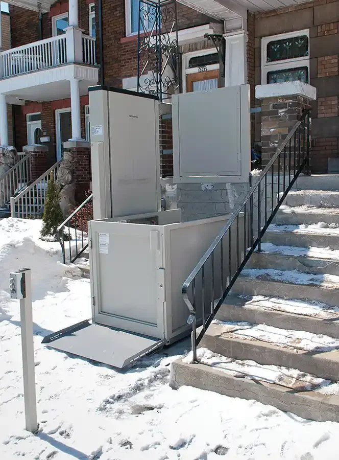 Outdoor wheelchair platform lift installed alongside residential steps in a snowy urban setting