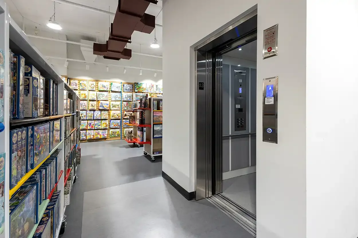 Open commercial elevator in a retail store aisle with shelving displays and exposed ceiling