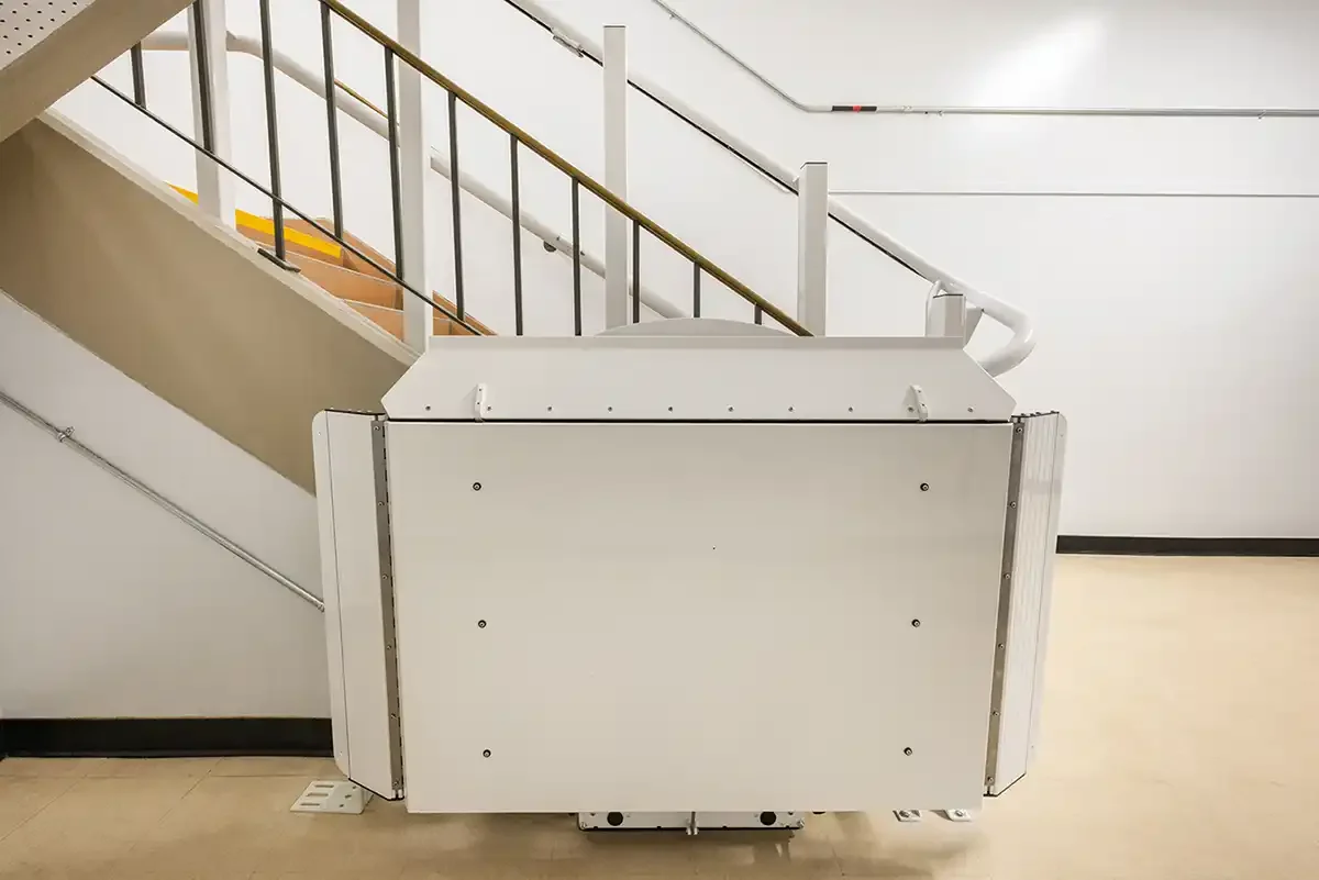 Folded inclined platform lift stationed at the base of a commercial staircase with metal handrails and light-colored flooring
