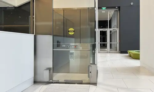 A V-1504 Vertical platform lift installed in a commercial setting, with glass doors.
