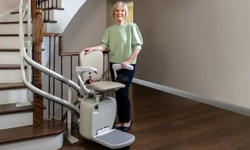 A smiling woman posing with her twin rail Savaria Stairfriend23 curved stairlift.