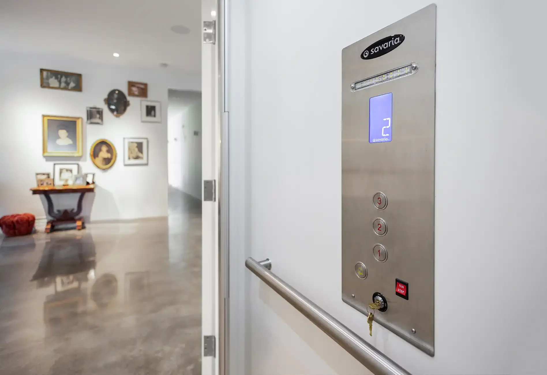 Savaria home elevator car operating panel (COP) with stainless steel finish, digital floor indicator, destination buttons, key switch, and alarm in residential hallway