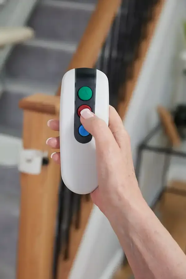 User holding Savaria Handicare stairlift RF remote control with green call button and red stop button for calling chair to different landings