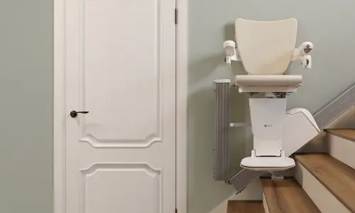 Stairlift with a folded vertical rail section positioned beside a closed door, showing the compact track design that tucks out of the way at the bottom of the staircase.
