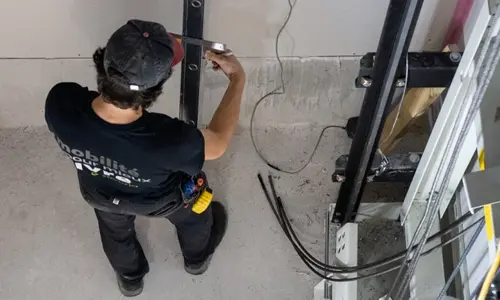 Elevator technician measuring and aligning a vertical guide rail inside a residential home elevator shaft during installation.