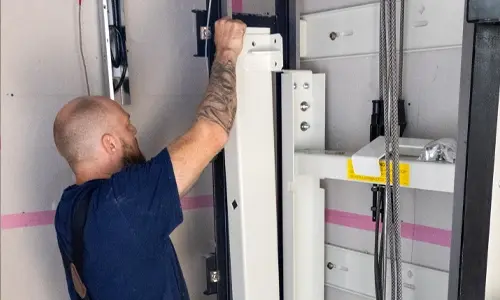 Elevator technician installing and securing vertical guide rail components inside a residential home elevator shaft during lift installation.