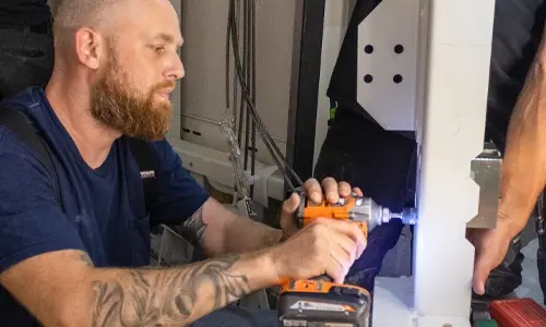 Elevator technician using a cordless drill to install structural components inside a residential home elevator shaft during lift construction.