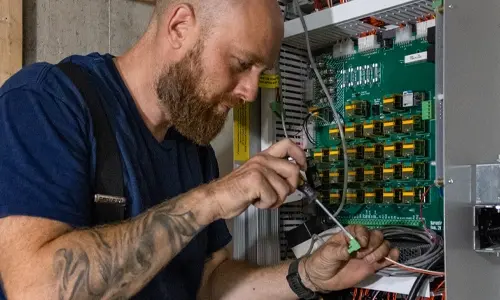 Elevator technician wiring and adjusting circuit boards inside a residential elevator control cabinet during installation and maintenance.