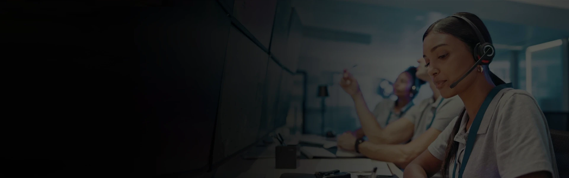 Customer support agents wearing headsets working at multiple monitors in a modern office
